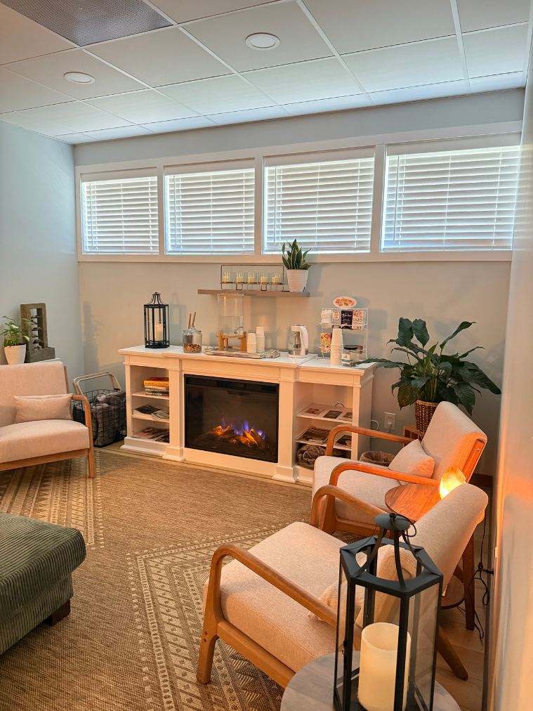 The relaxation room at Allure with a fireplace, upholstered chairs, plants and a refreshment station